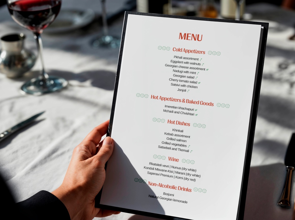 A hand holding an open printed menu folder with red Georgian-styled type